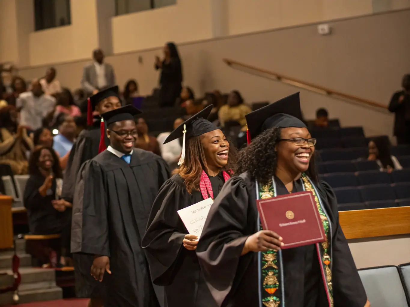 A photograph of a graduate of Maven School of Interior Decoration and Design receiving their certificate at a graduation ceremony, with faculty members and proud family members in the background.